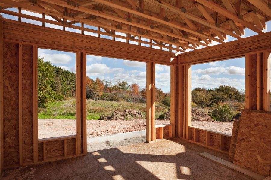 Wood-framed home addition under construction with large window openings and exposed roof trusses